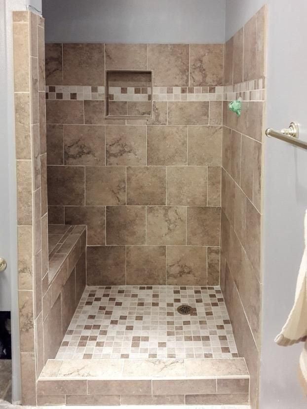 Tiled shower stall with a built-in bench and recessed shelf. Tan and brown tiles, mosaic floor.
