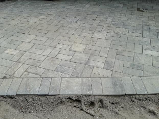 Gray stone paver patio with a border, edges next to dirt.