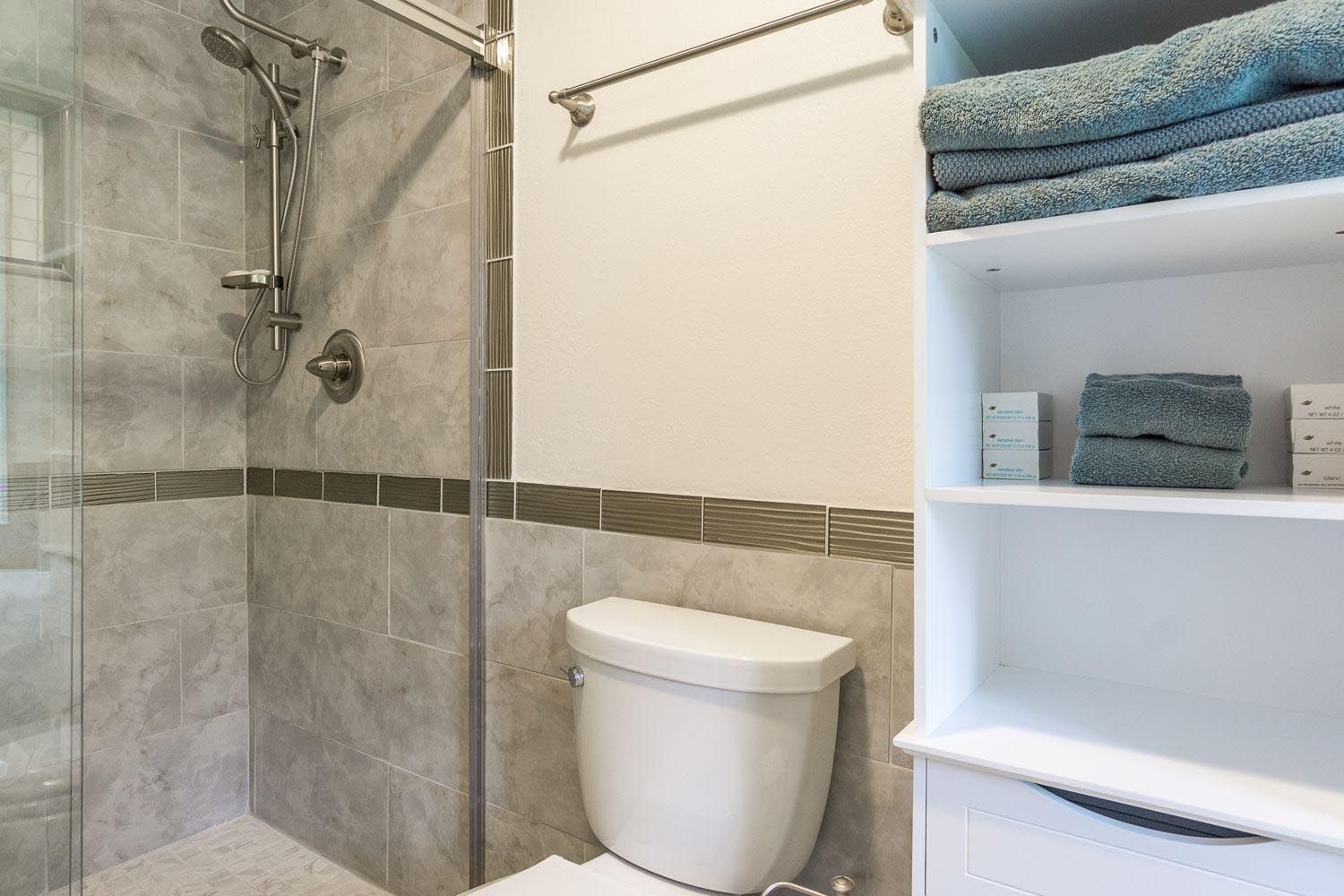 Bathroom with tiled shower, toilet, and shelving with towels.