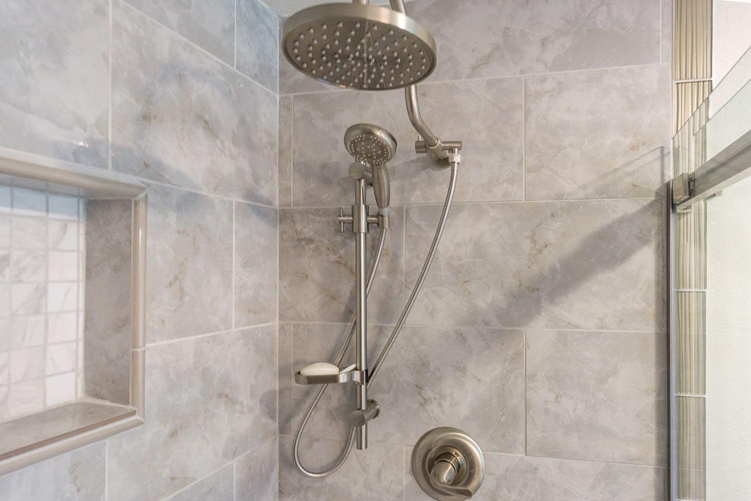 Shower with large overhead showerhead and handheld shower, gray tiled walls.