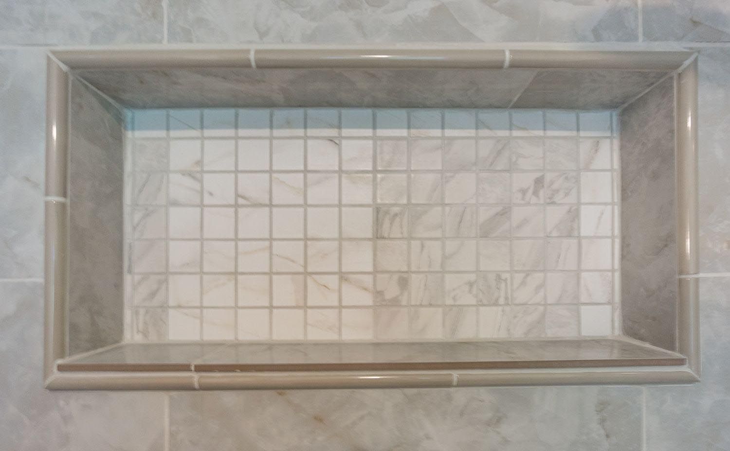 Recessed shower shelf with marble tile and gray border.