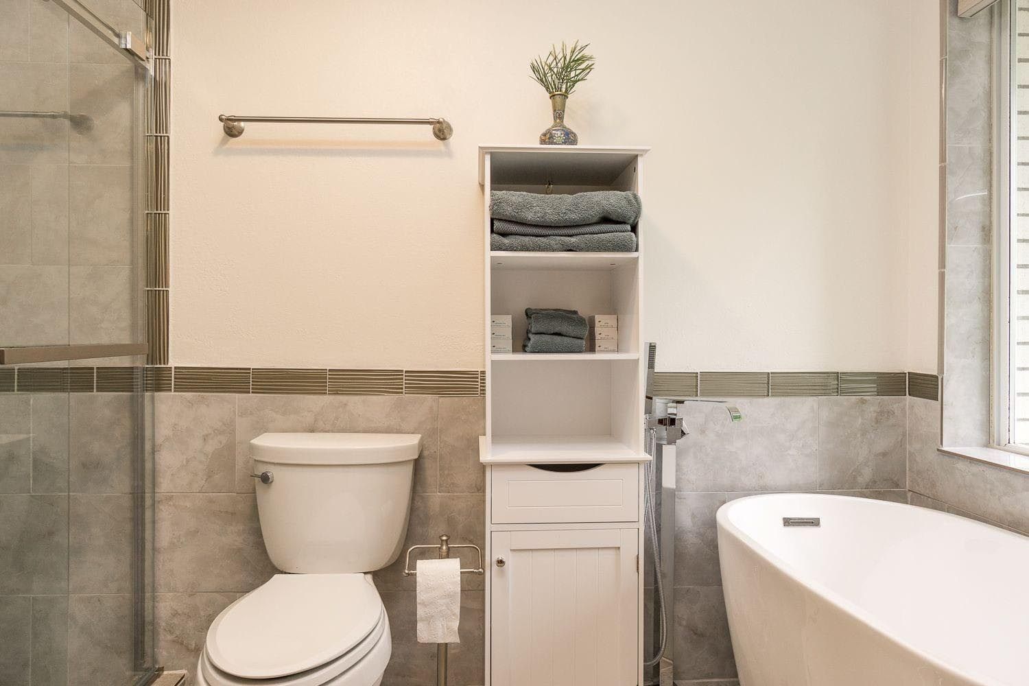 Bathroom with a white toilet, storage cabinet with towels, and a bathtub.