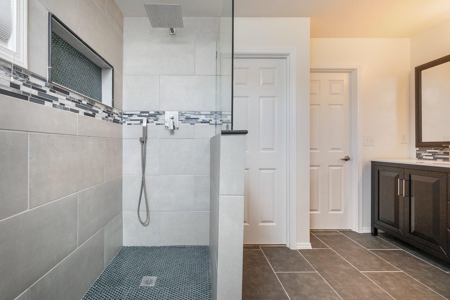 Modern bathroom with gray tiled shower and dark vanity.
