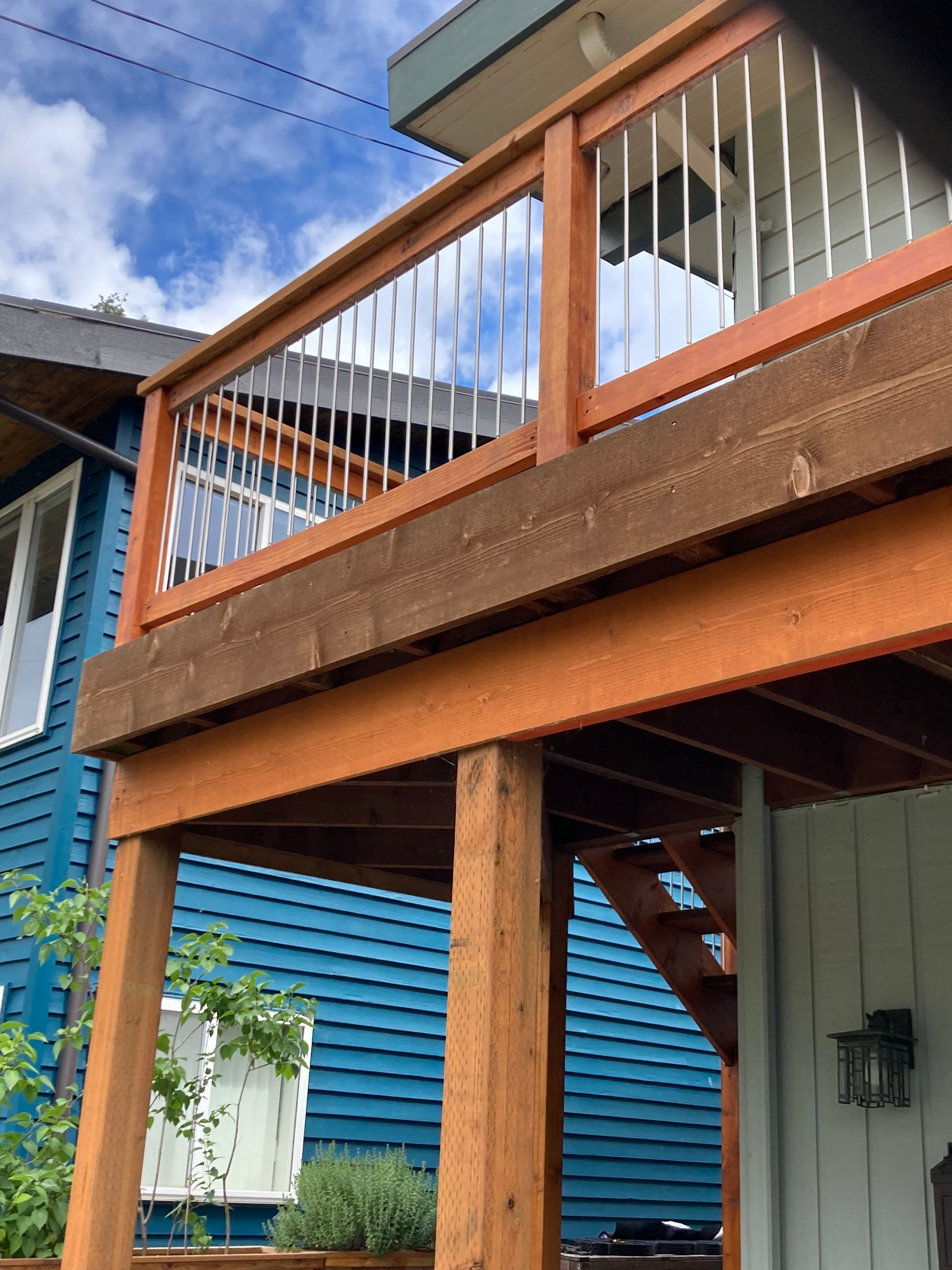 Wooden deck with stainless steel railings, attached to a blue house.