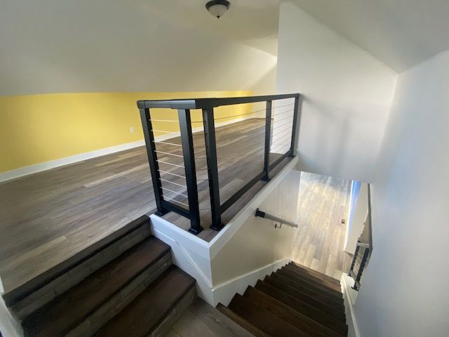 Wooden staircase leads to a loft with dark railing, light wood floors, and yellow and white walls.