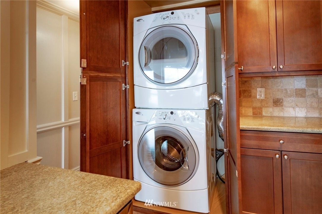 Stacked washer and dryer unit inside a wooden cabinet in a kitchen.