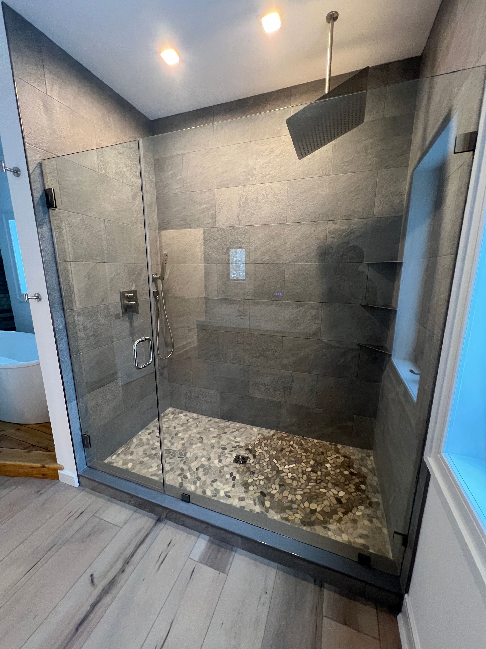 Cleaner scrubbing a white bathtub in a bright bathroom with blue gloves and cleaning supplies nearby