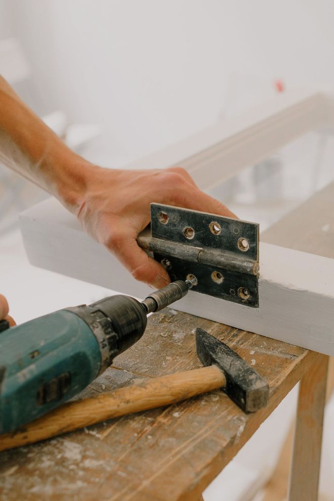 Person using a teal power drill to screw into a wooden plank outdoors