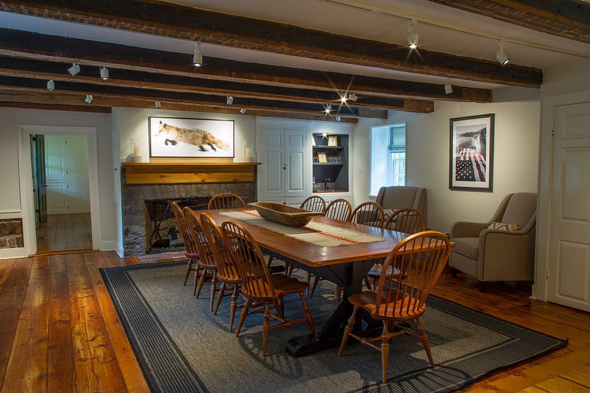 Dining room with large wooden table, chairs, fireplace, and exposed beams.