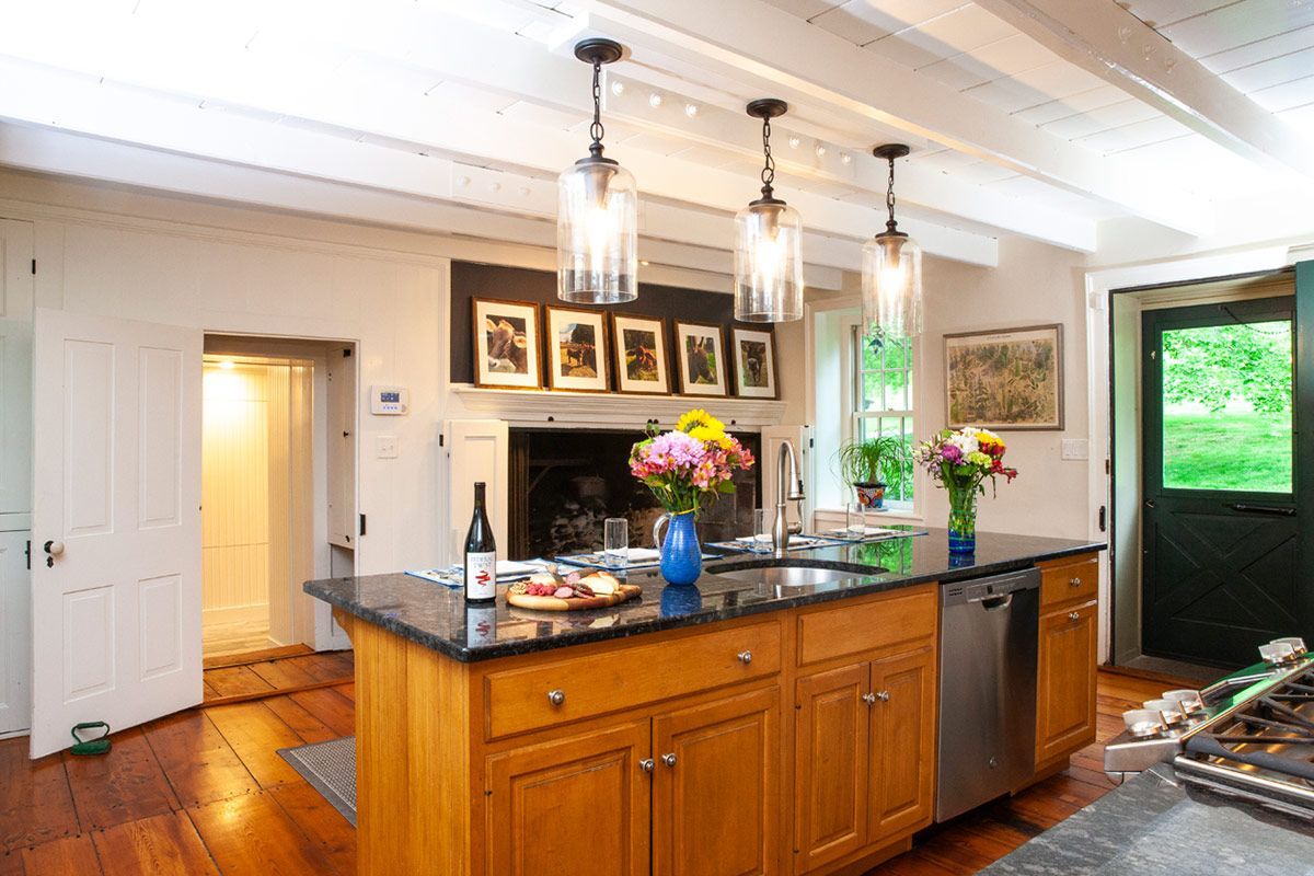 Kitchen with wooden cabinets, island, black countertop, open doorway, three pendant lights, flowers.