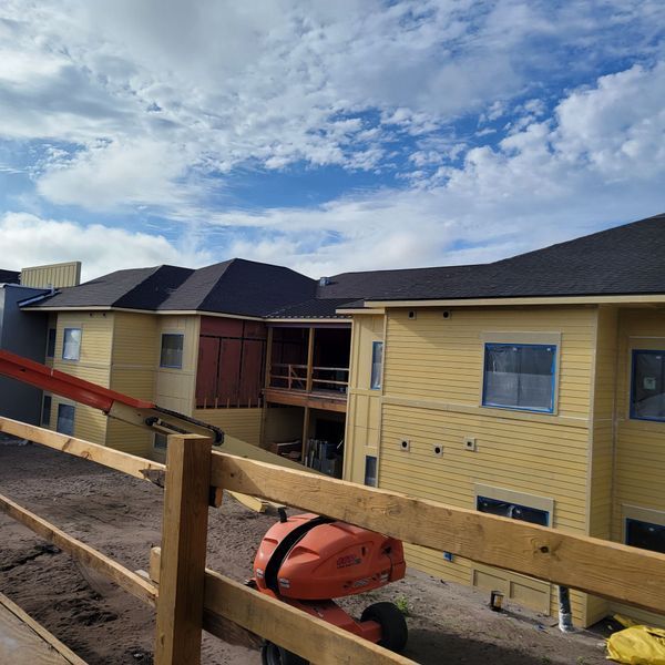 Construction site view: yellow building with black roof, wooden framework, lift, blue sky.