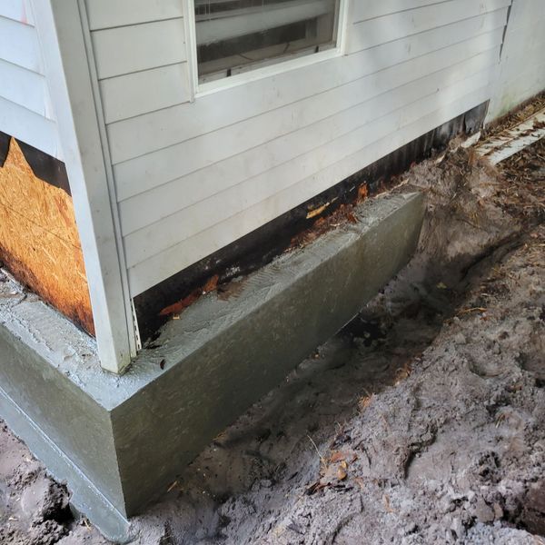Concrete foundation wall of a house, newly poured against siding, in an excavated area.