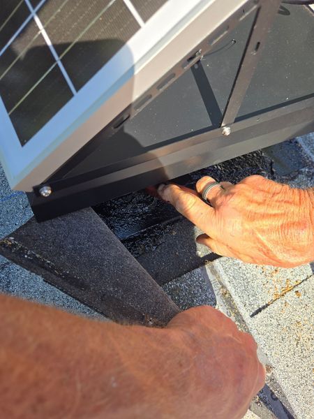 Hands installing solar panel on a rooftop, pointing at the base.