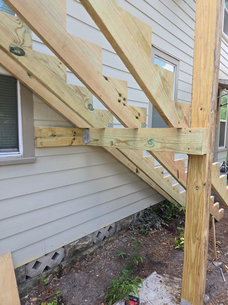 Wooden staircase under construction, attached to a light-colored house.