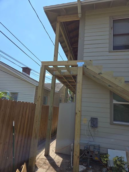 Wooden deck under construction on the side of a beige house, next to a brown fence.