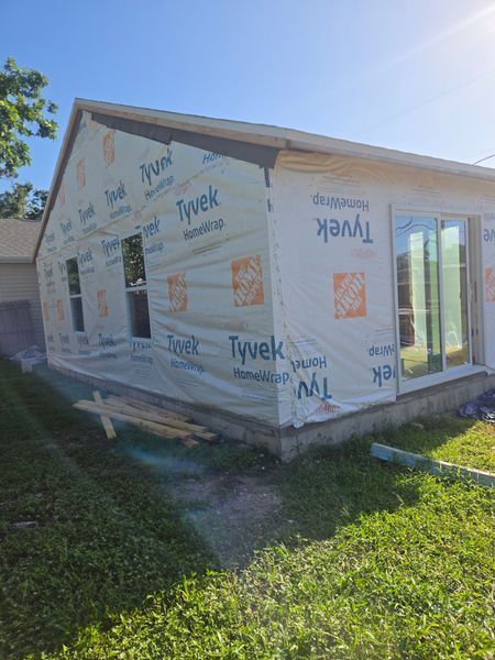 House under construction, exterior view, Tyvek wrap, windows and sliding door, sunny day.
