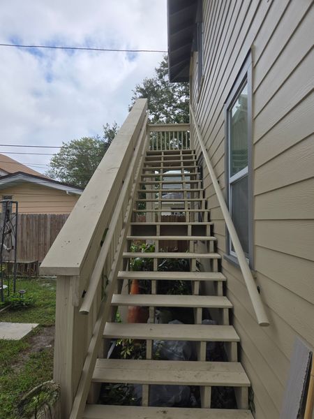 Wooden outdoor staircase leading up the side of a beige house, with a railing on both sides.