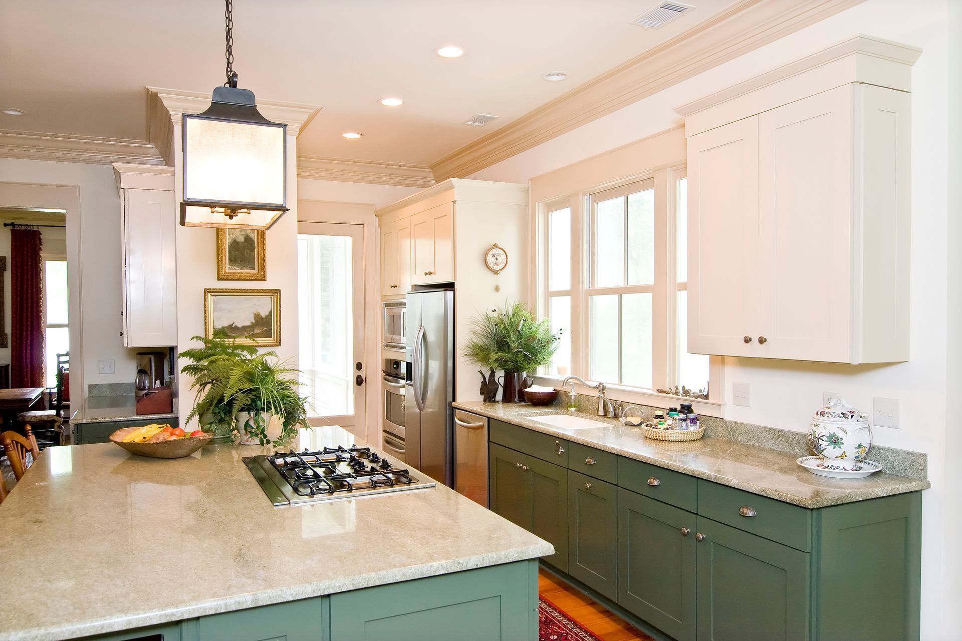 Kitchen with green cabinets, light countertop, stainless steel appliances, and island with a cooktop.