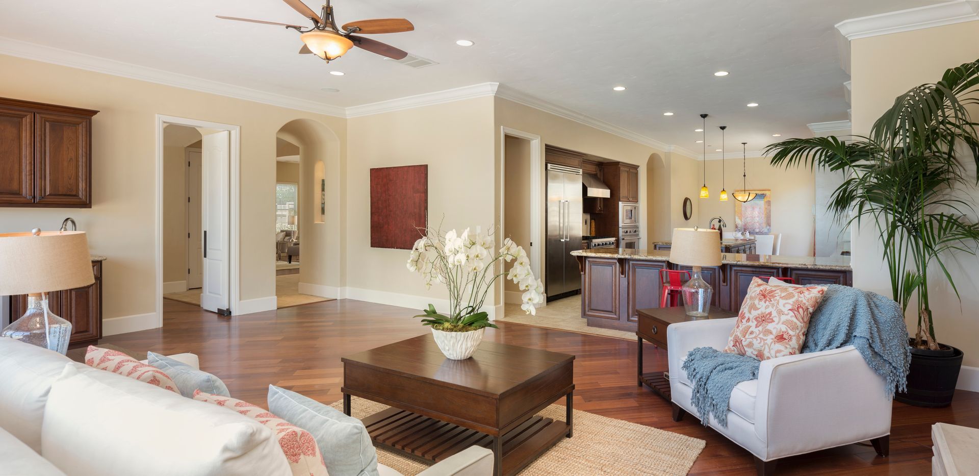 Spacious living room with hardwood floors, a white sofa, and a large plant next to a white armchair.