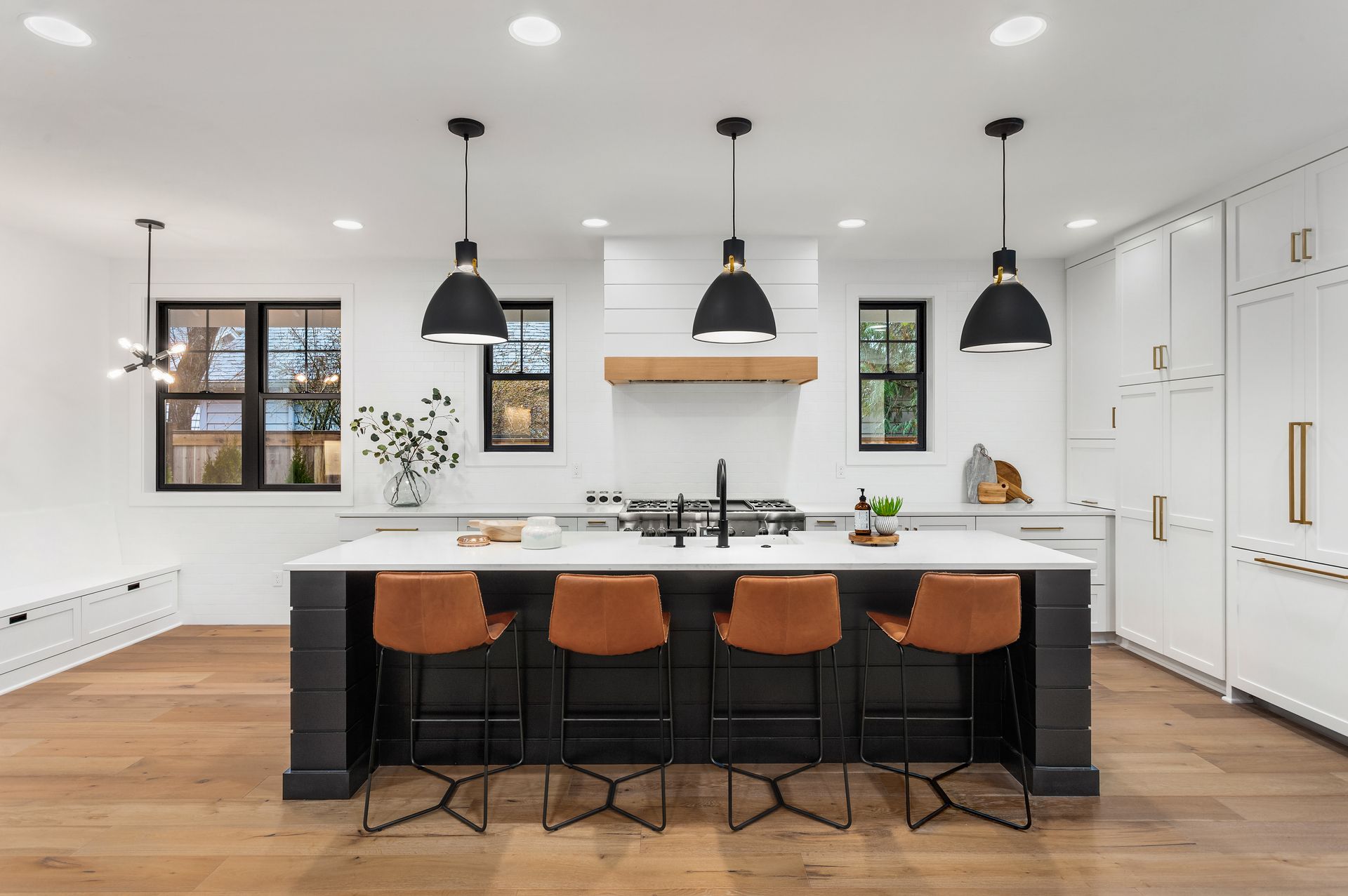 Modern kitchen with a black island, brown bar stools, and black pendant lights.
