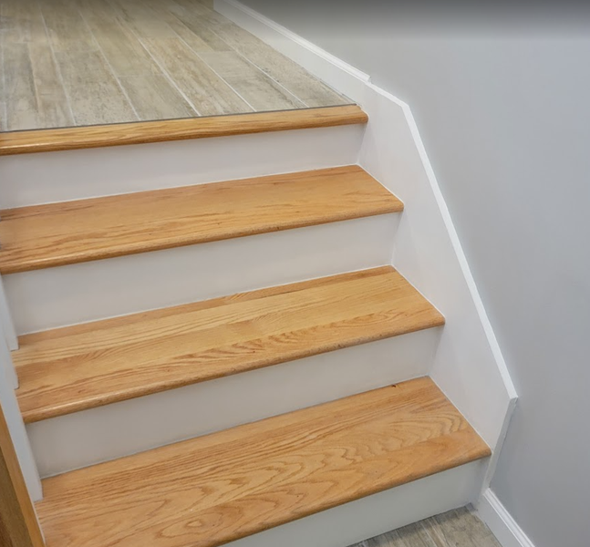 Wooden staircase with light brown treads, white risers, and gray wall.