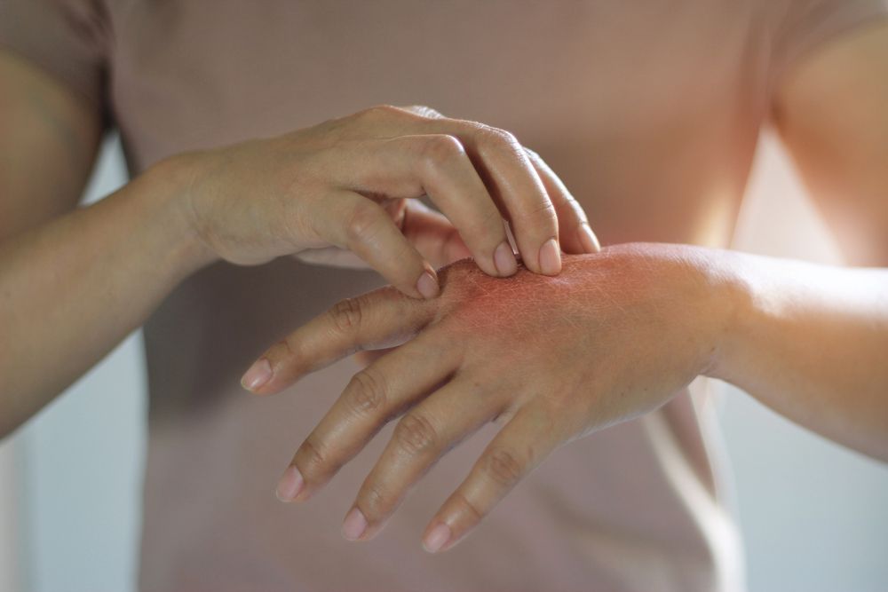 Mani che applicano una lozione sulla mano di un'altra persona, su uno sfondo tenue.