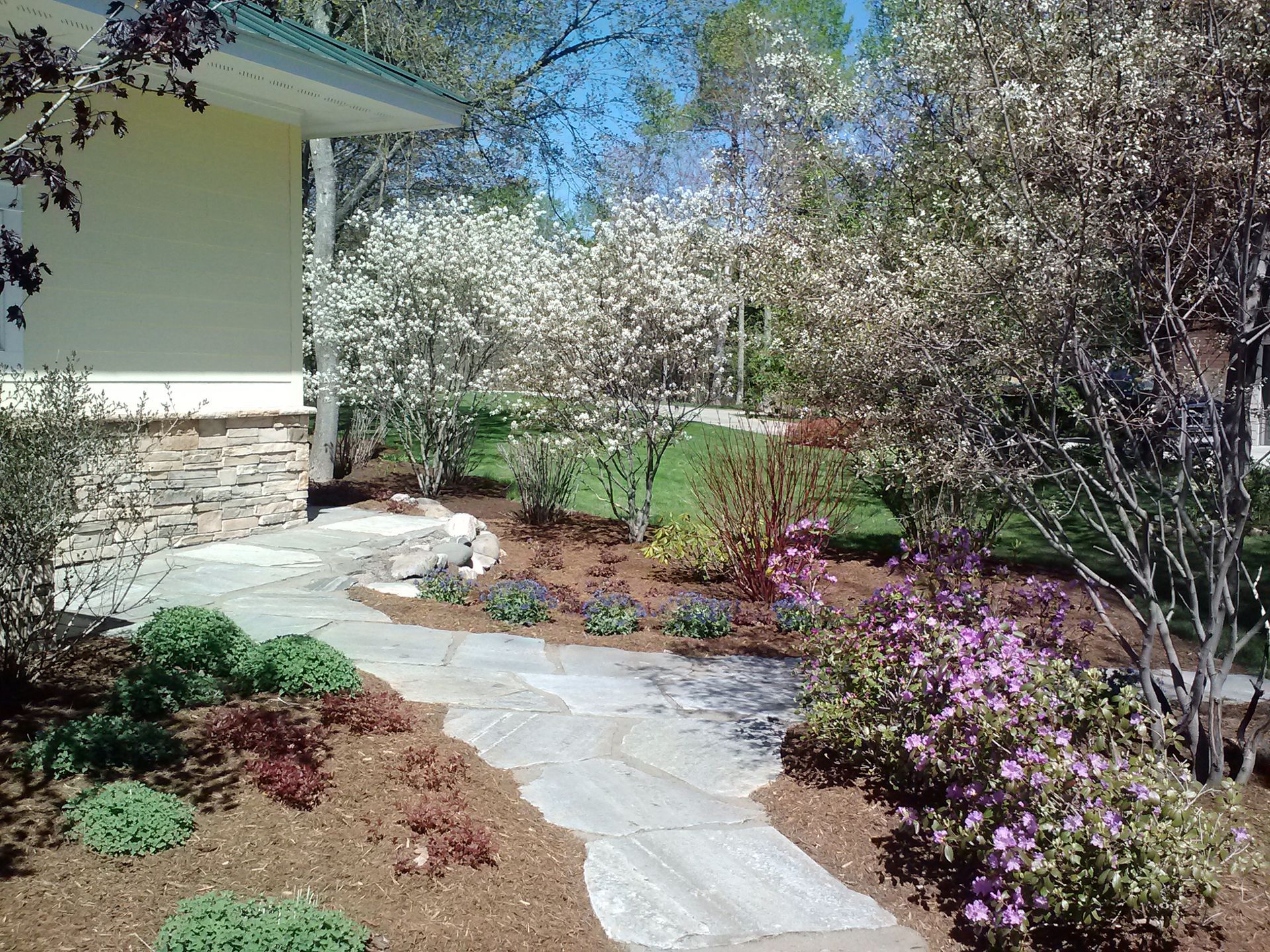 An aerial view of a person installing new sod turf next to a gravel flower bed with small plants and stone steps.