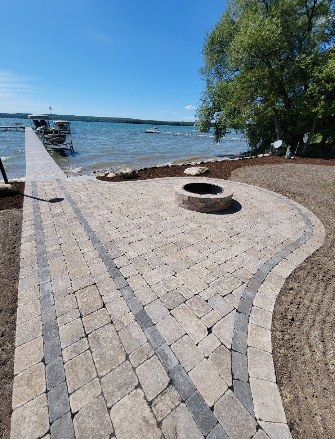 A curved garden retaining wall made of tan, textured stone blocks borders a lush green lawn and flower bed.