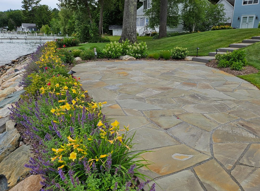 Stone stairs ascend through a lush garden with white and pink flowering shrubs and a stone retaining wall.