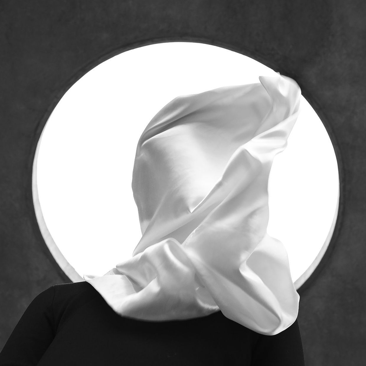 White fabric billowing in front of a bright circle, against a dark background.