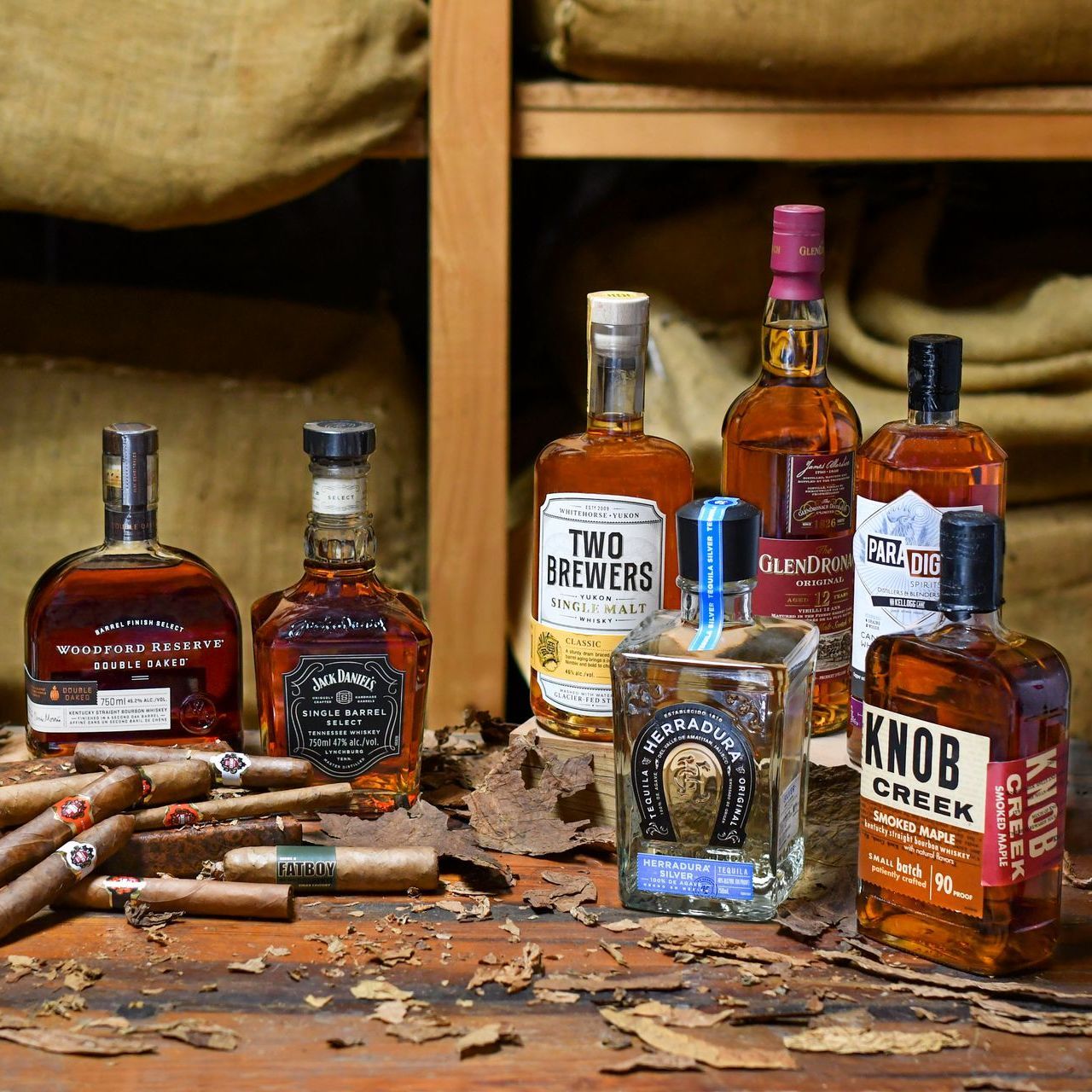 Bottles of liquor, including whiskey and tequila, with cigars on a rustic wooden surface.