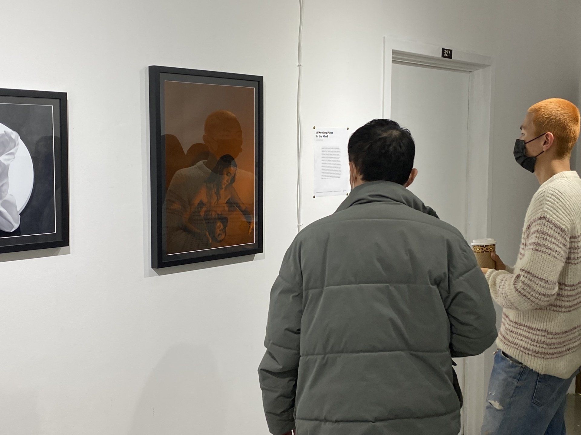 Two people viewing art in a gallery. The center piece has a warm orange hue, one is wearing a mask.