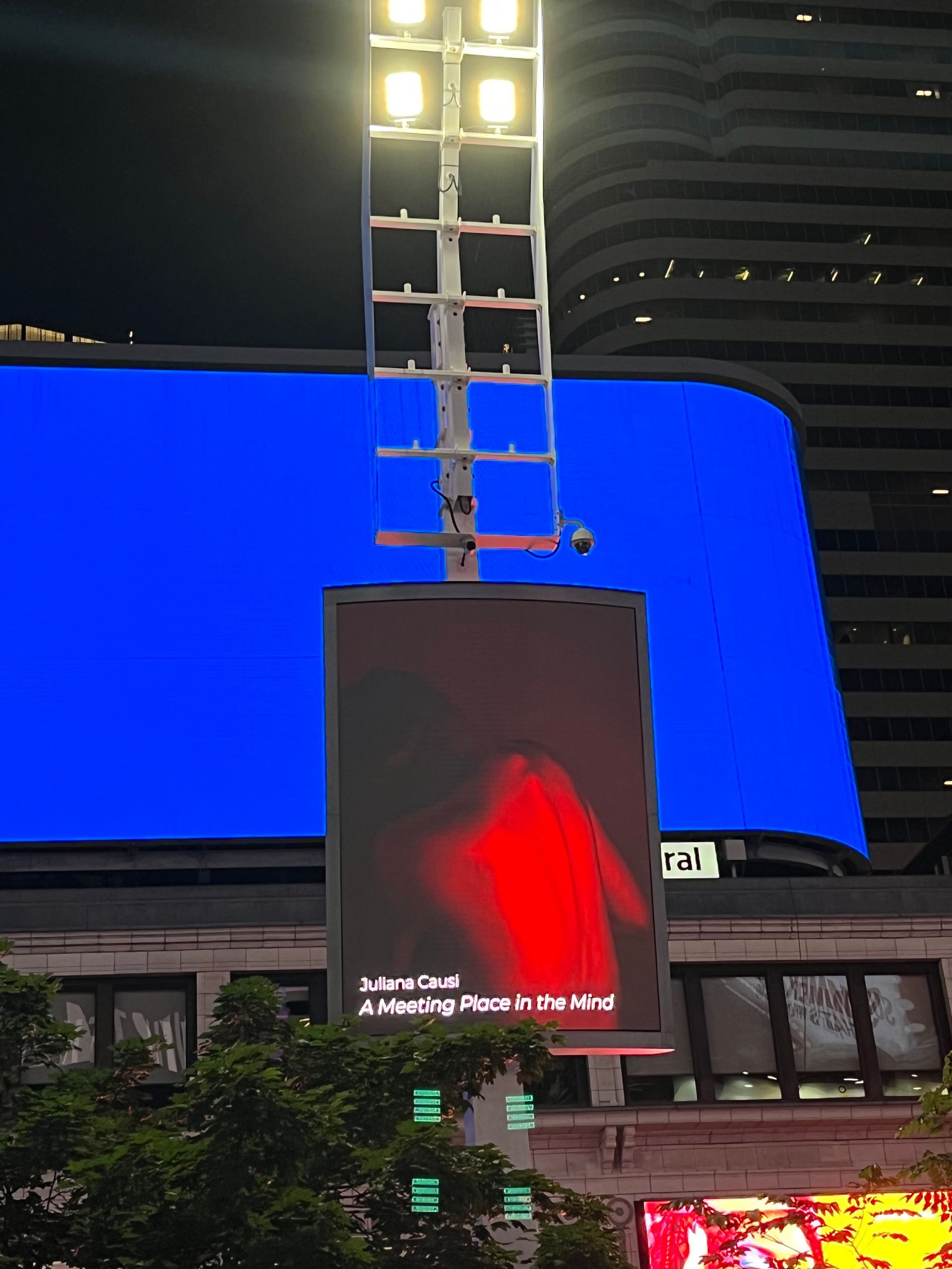 Large blue screen with a red advertisement, lit by bright square lights at night.