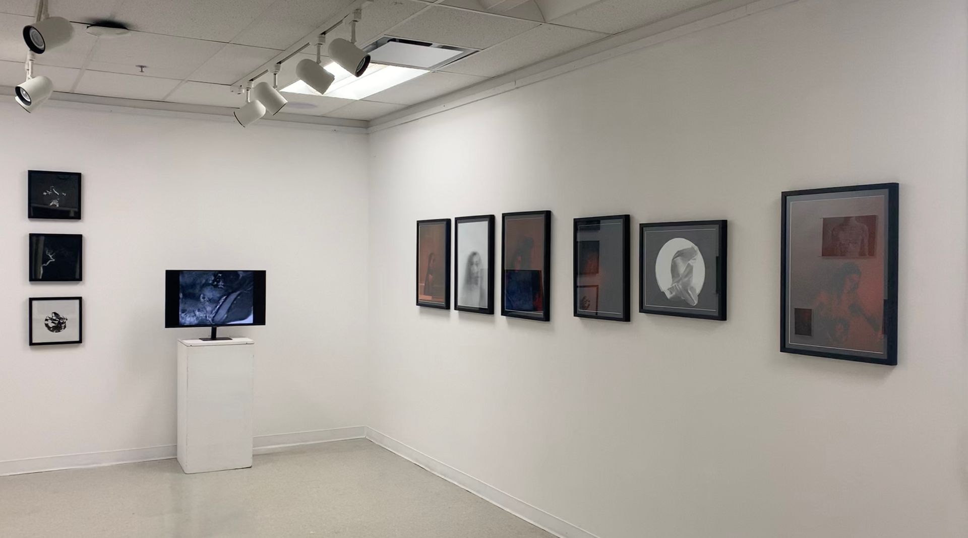White art gallery with framed artworks on walls, a TV, and spotlights.