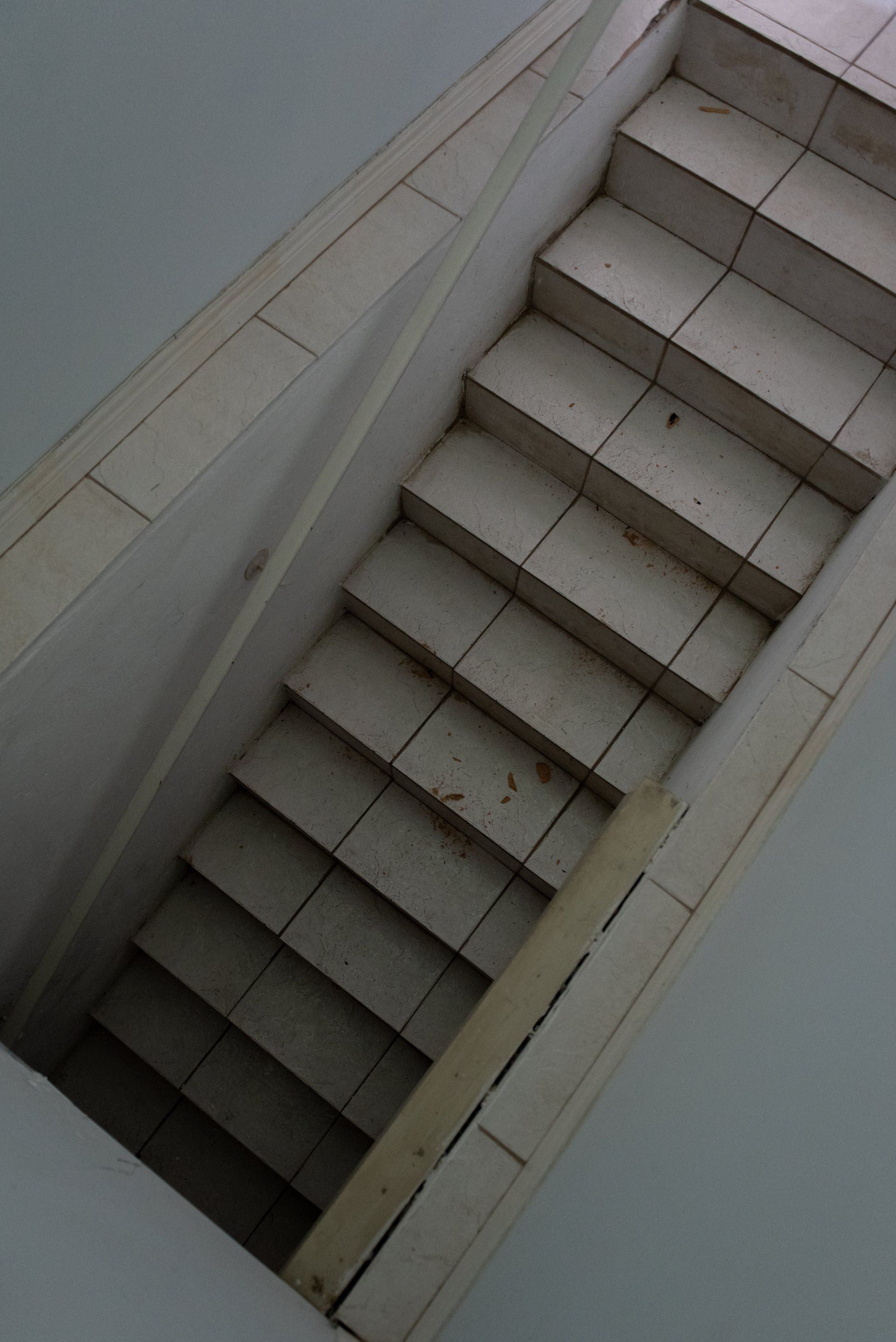 Staircase leading downwards. White tile steps and walls in an enclosed space.