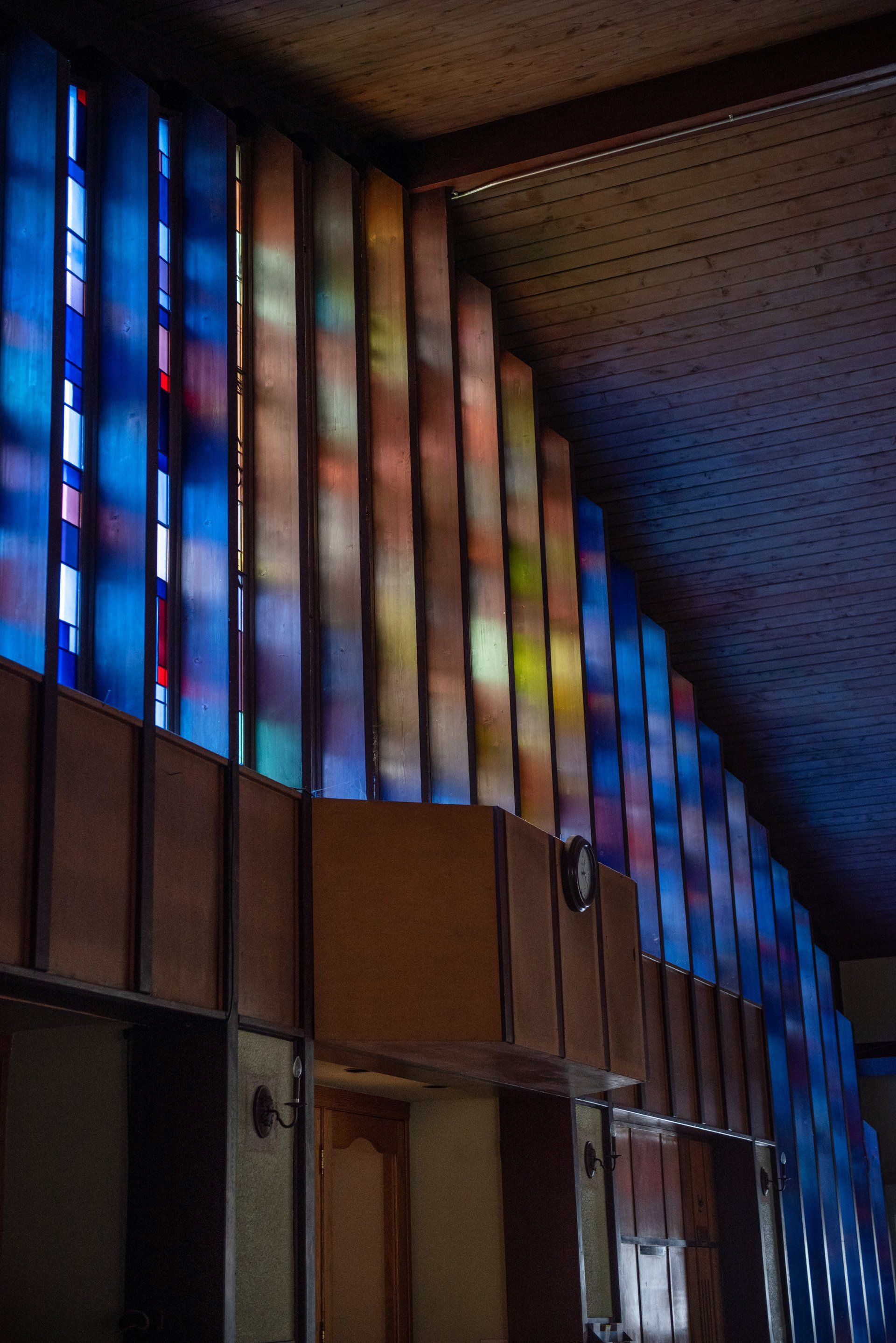 Colorful stained glass windows above a wooden structure, casting light onto a textured ceiling.