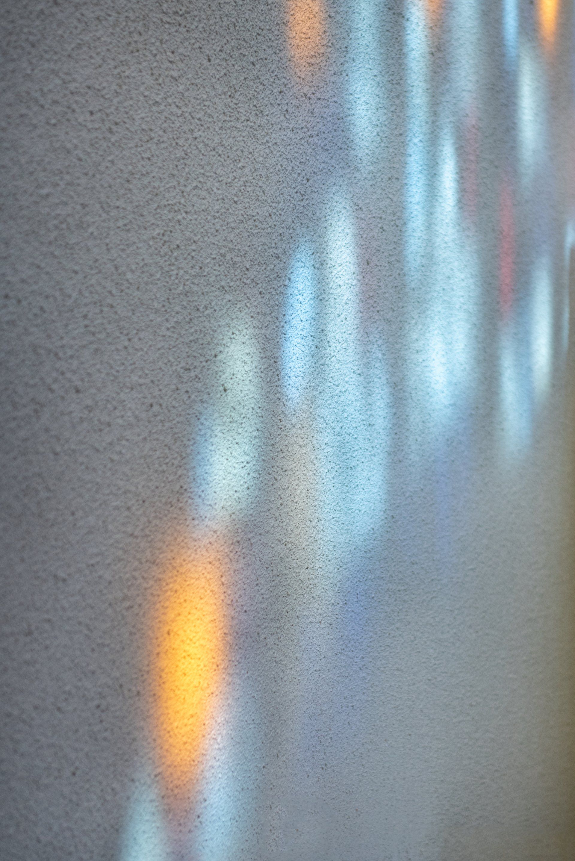 Colorful light reflections on a textured white wall.