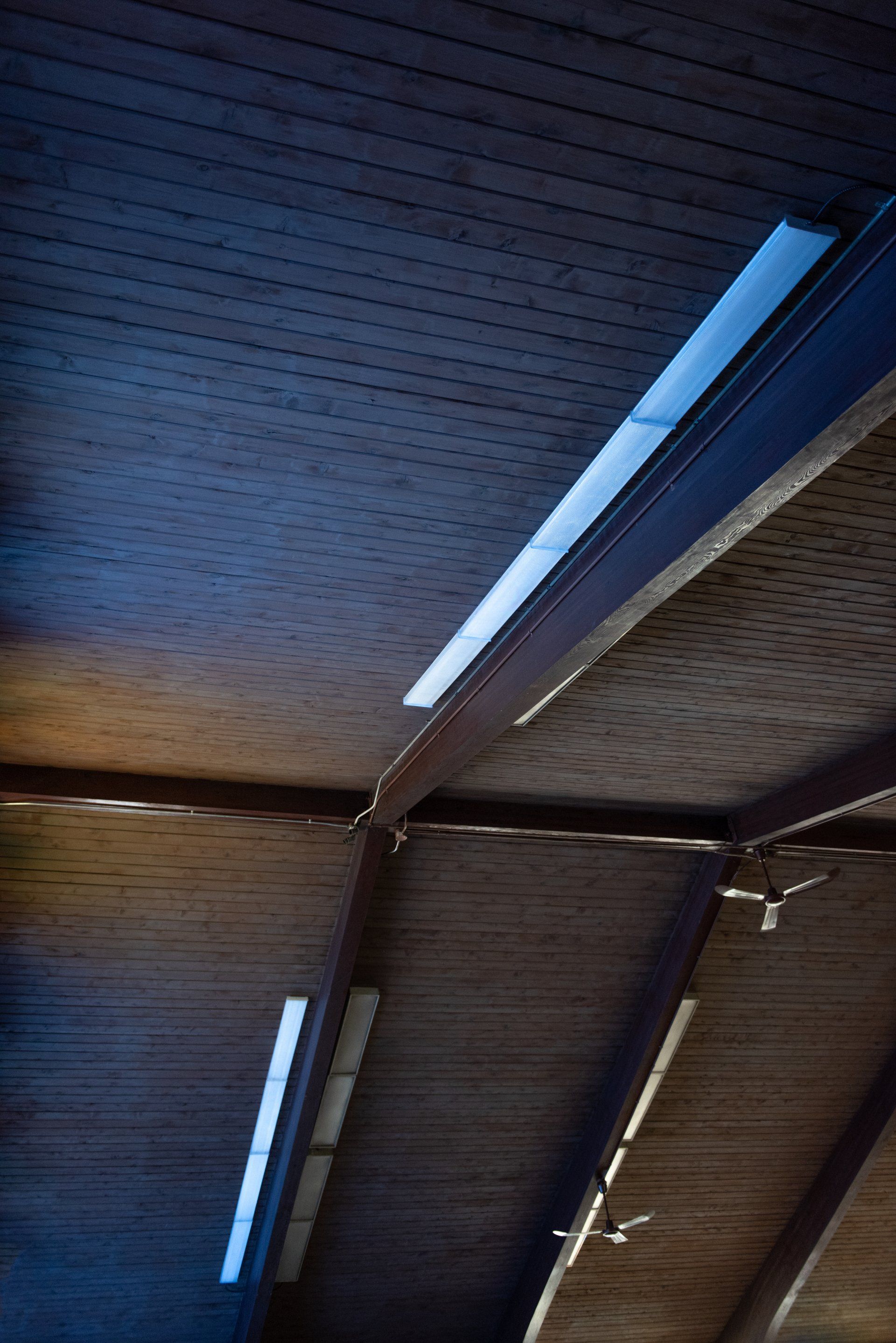 Low-angle view of a wooden ceiling with exposed beams and recessed fluorescent lighting.