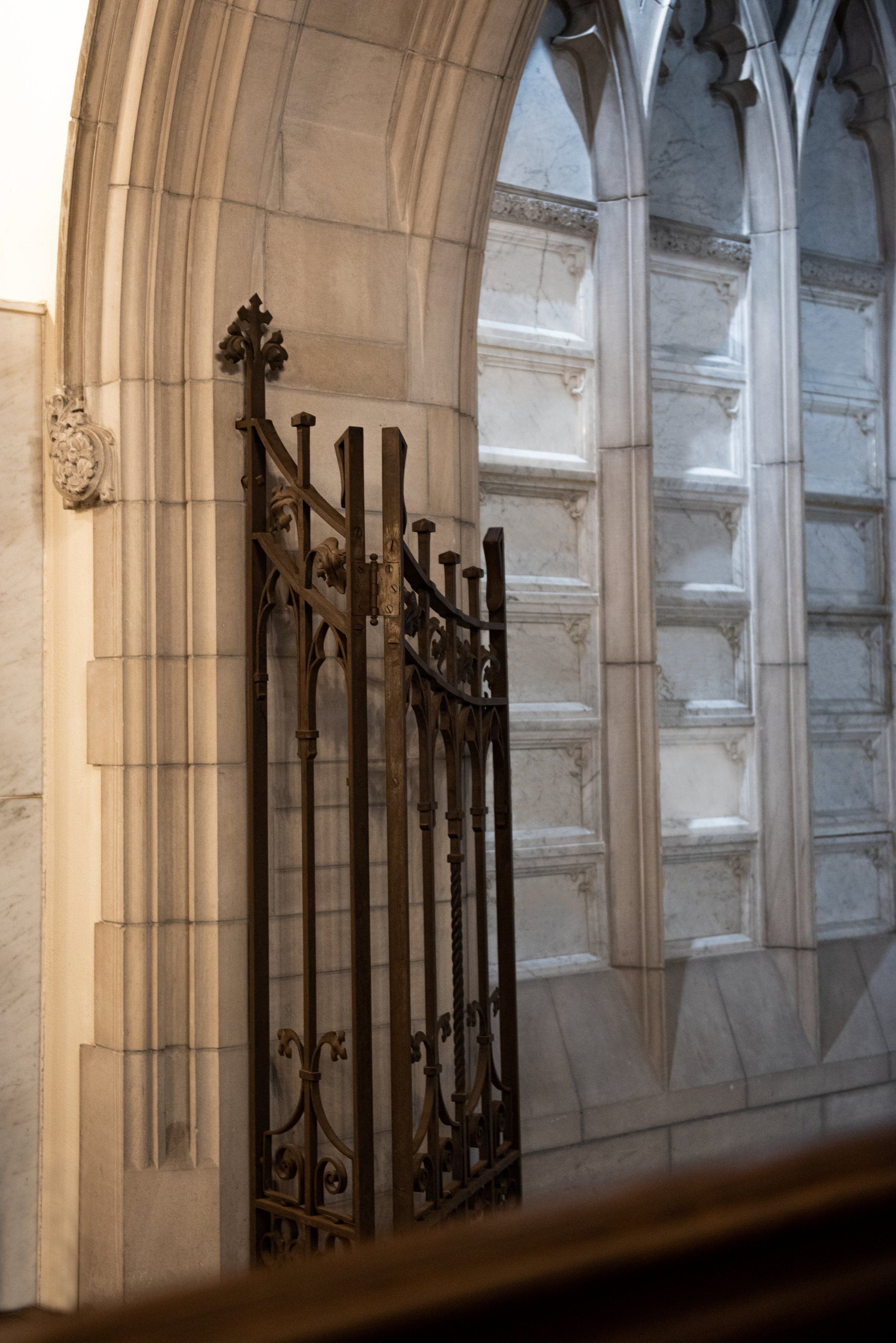 Ornate metal gate in a stone alcove with arched windows, inside a building.