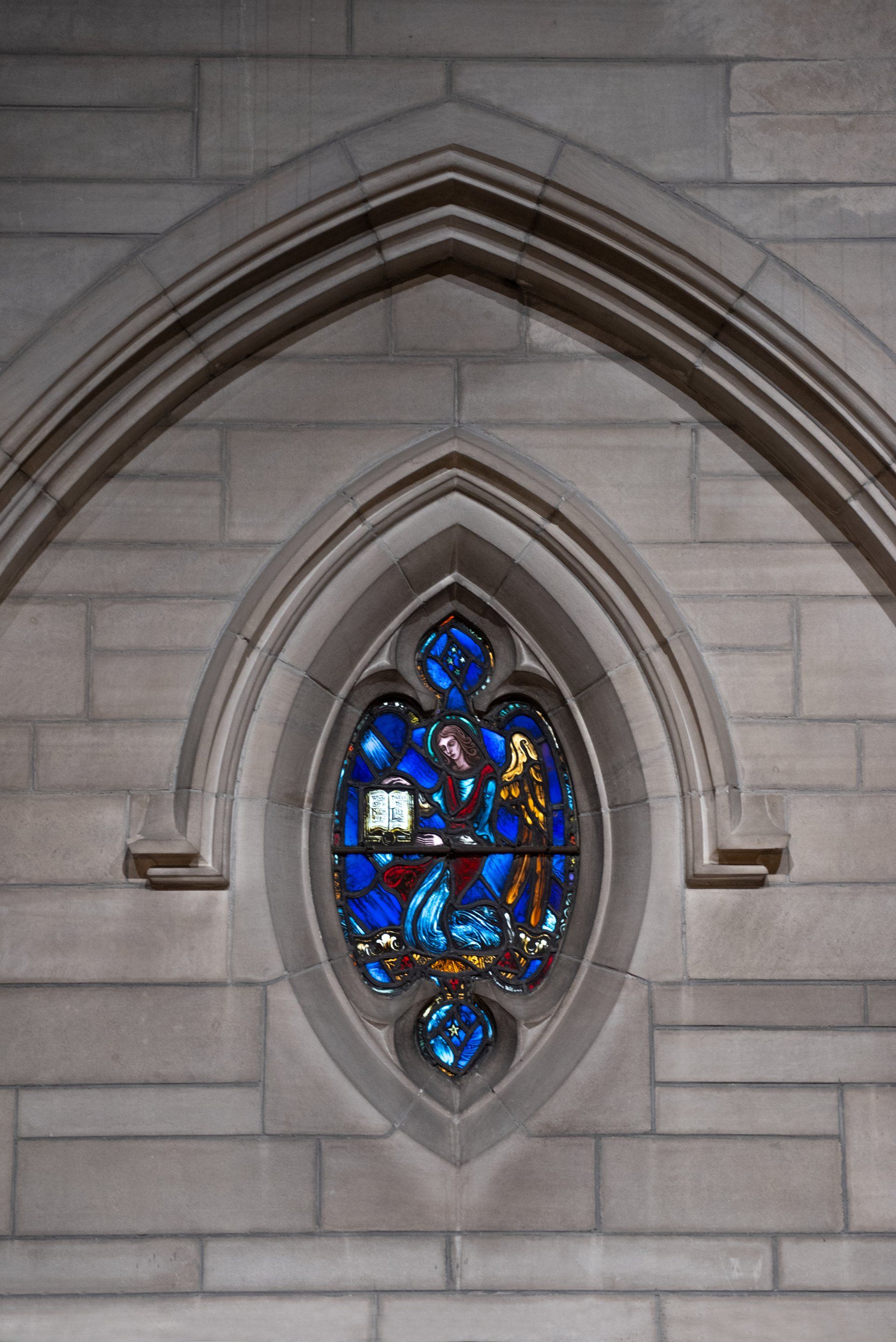 Stained glass window, blue and gold, within a stone wall arch.