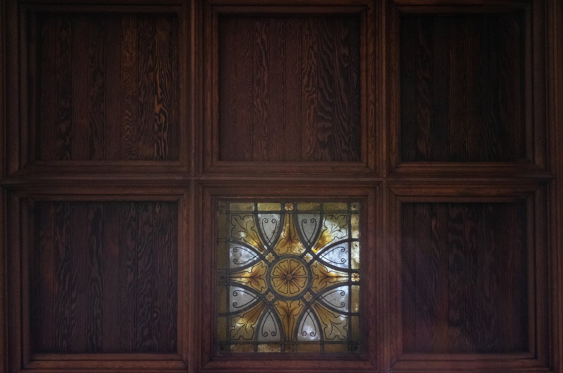 Wood paneling with a stained-glass window in the center, featuring a gold and white floral design.