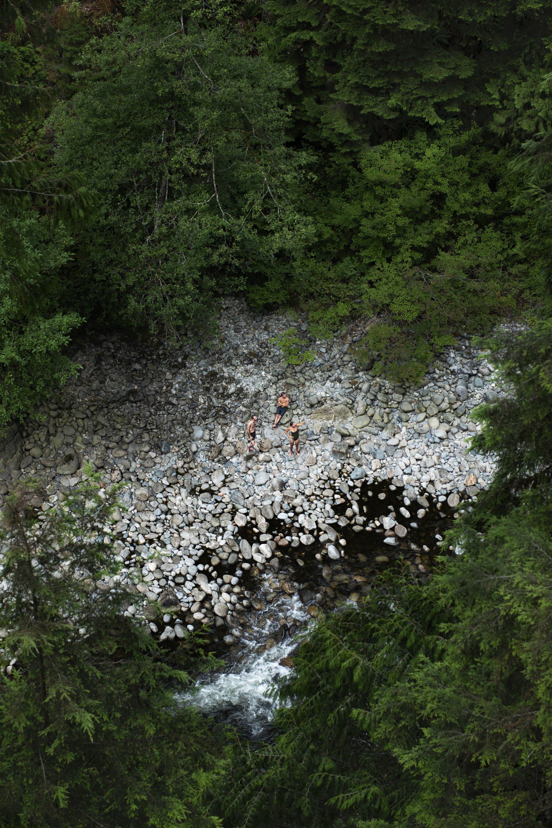 Rocky riverbed with a flowing stream, surrounded by trees. Several people are near the stream.