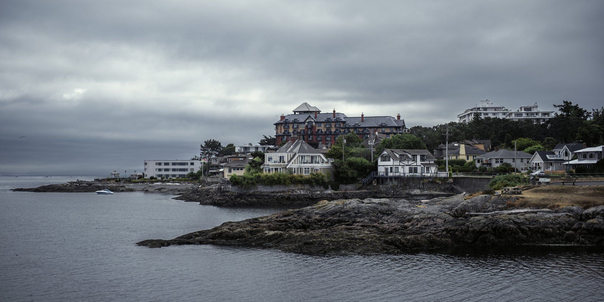 Coastal town under a cloudy sky. Houses and buildings on a rocky shore, ocean in the foreground.
