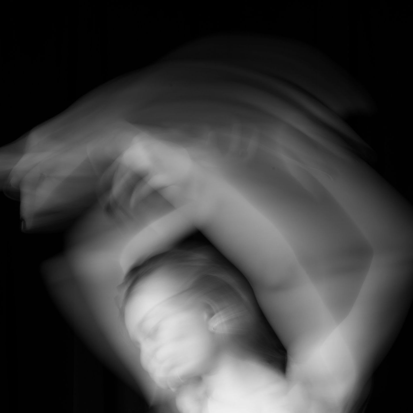 Blurred, black and white photo of a person moving. Arms raised over head, face obscured by motion blur.