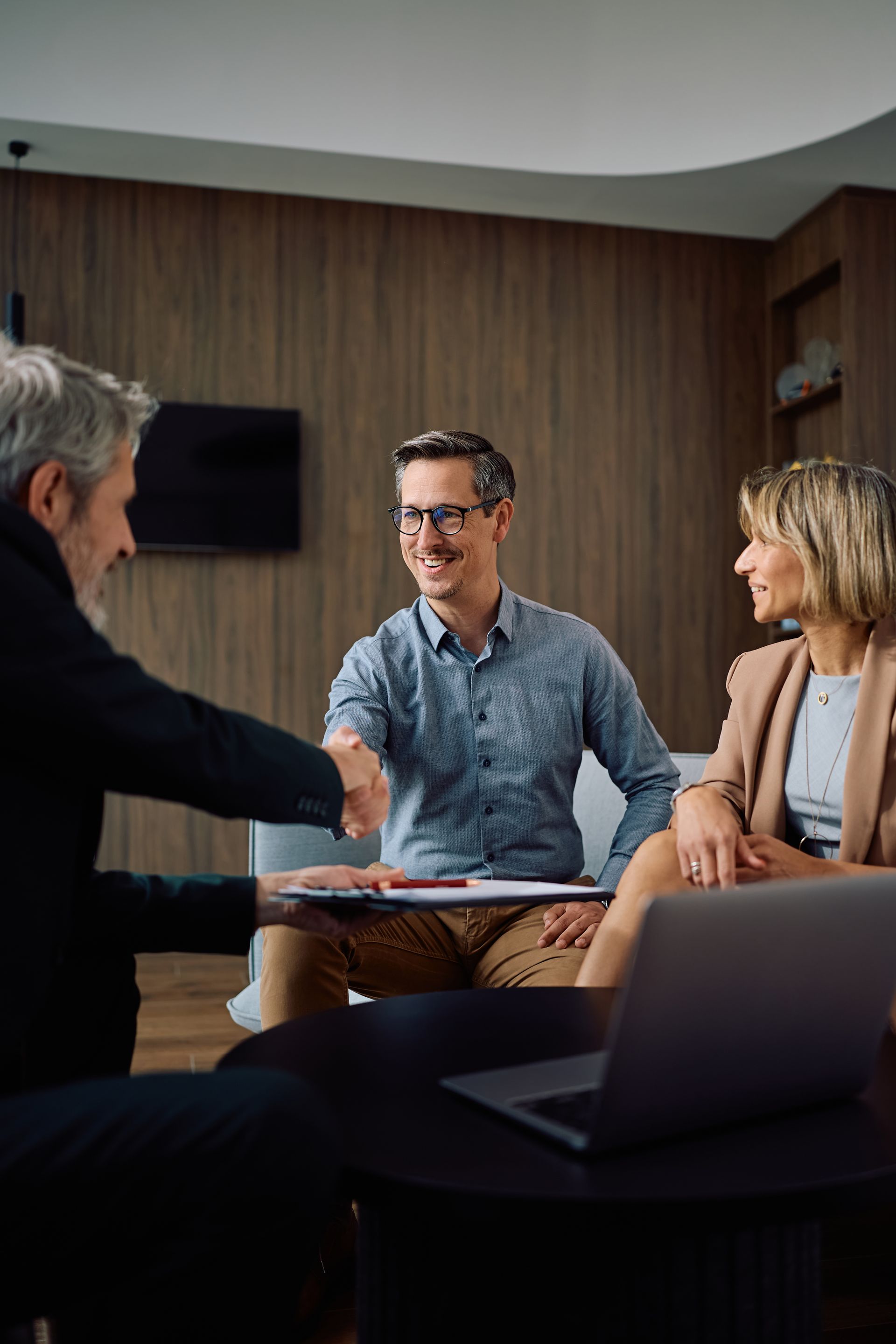 Three people in a meeting room discussing documents around a table with a laptop in the foreground