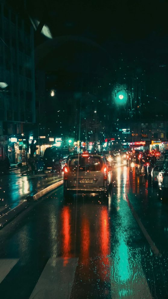 Rainy city street at night with traffic lights reflecting on wet pavement and cars driving ahead