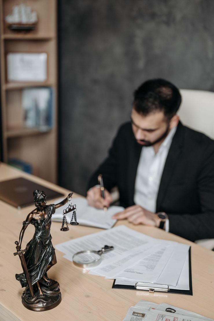 Lawyer writing at desk with Lady Justice statue and papers in a office