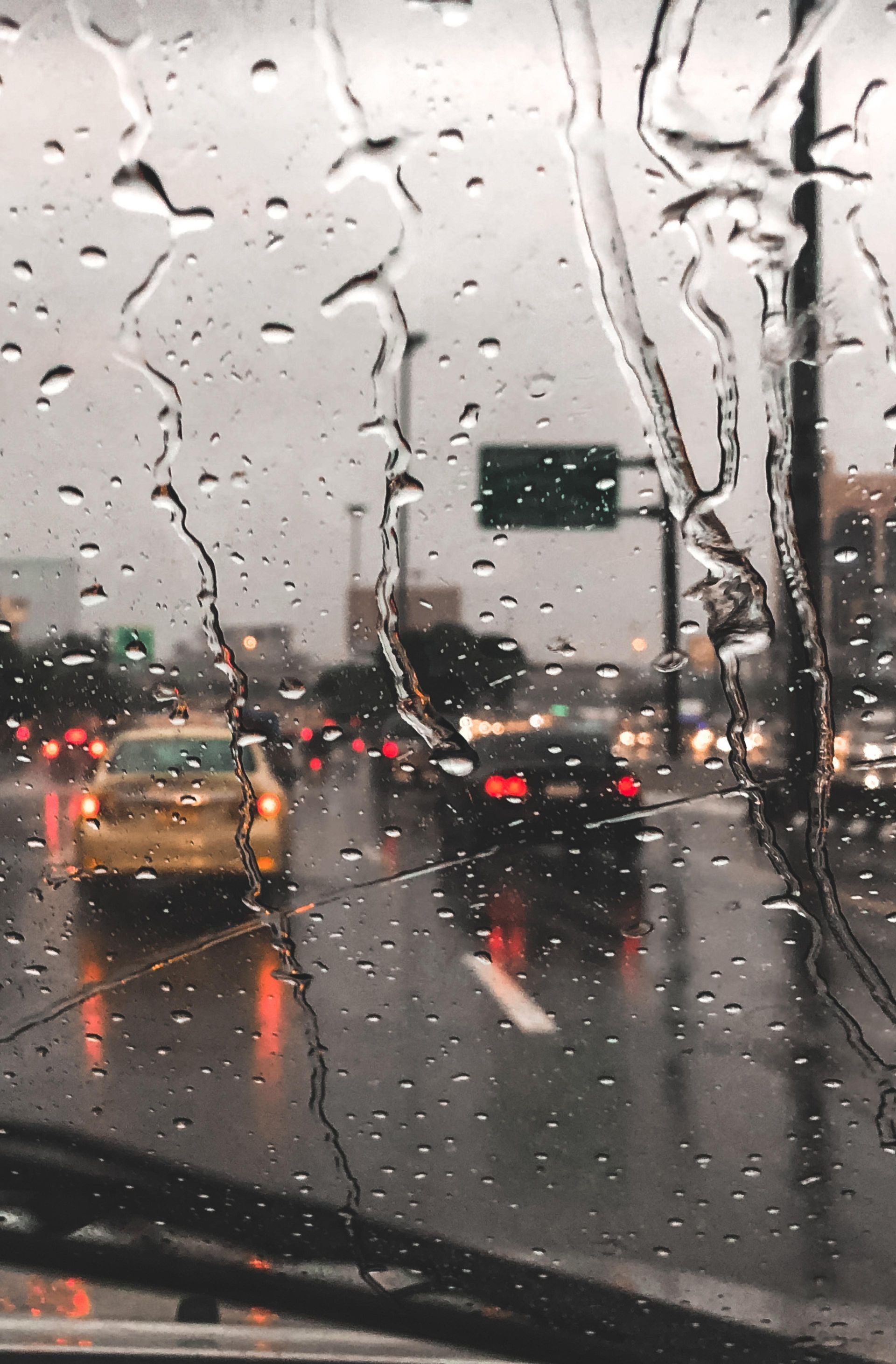 Rainy highway traffic through a wet windshield, with blurred cars and red brake lights ahead.