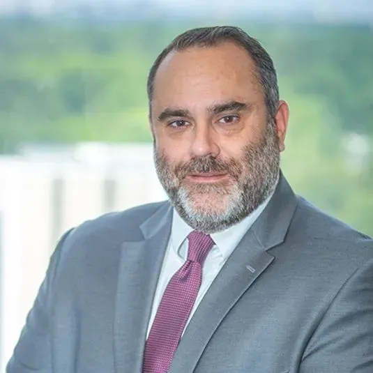 Man in gray suit and maroon tie, looking at the viewer, with a full beard, in an office setting.