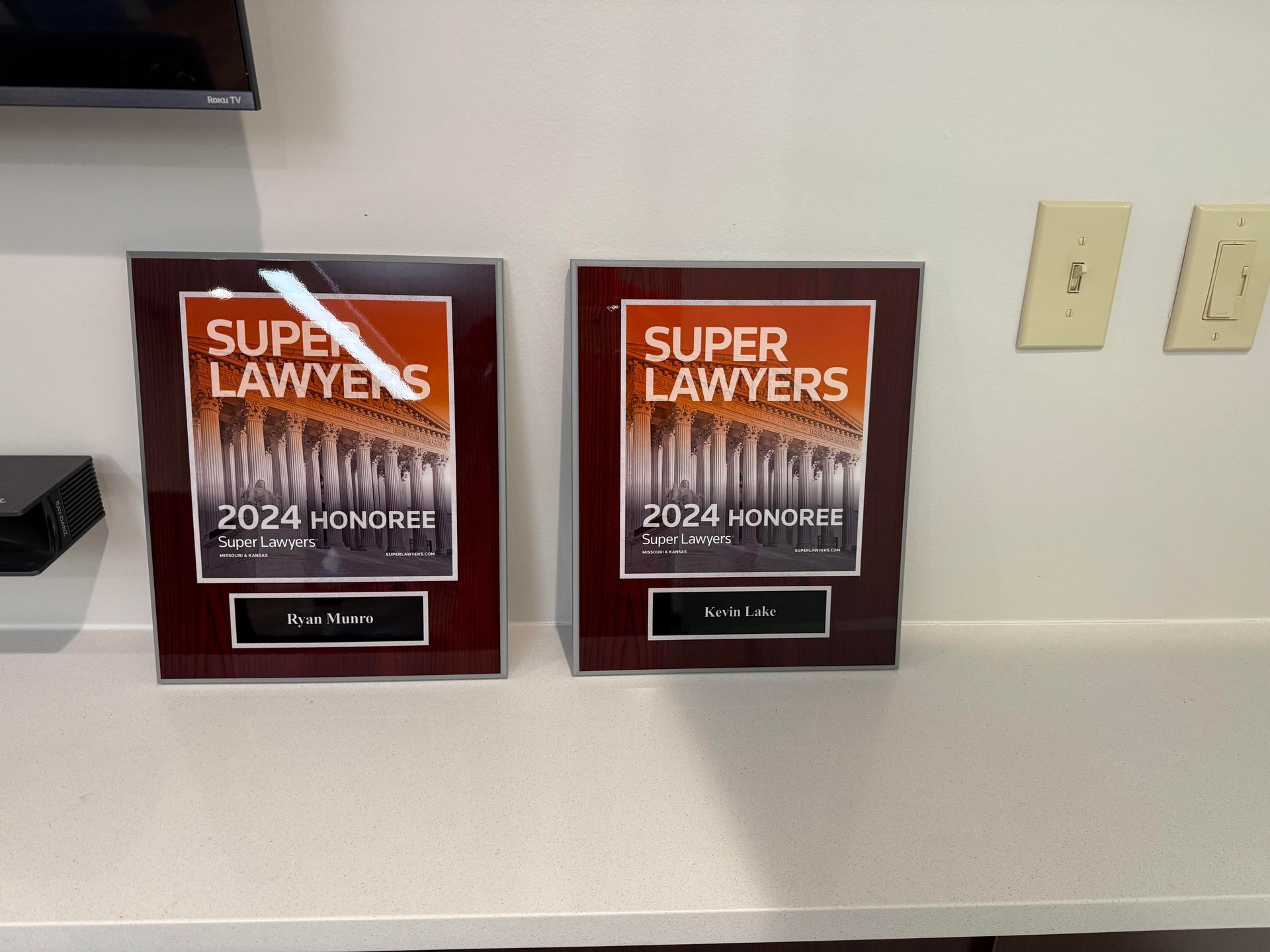 Two framed "Super Lawyers" awards from 2024 on a counter, with wall and outlets in the background.